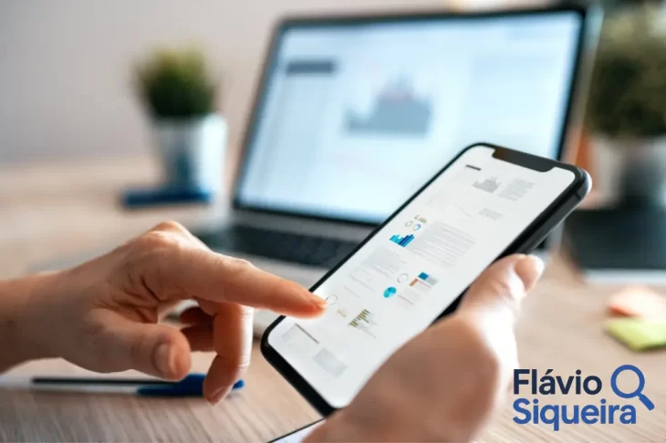 Pessoa usando app de finanças no celular, com gráficos exibidos na tela e notebook ao fundo, simbolizando controle financeiro digital e organização pessoal.