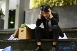 Homem sentado em frente a um prédio com caixa de pertences, demonstrando angústia após demissão, simbolizando a importância do seguro-desemprego.