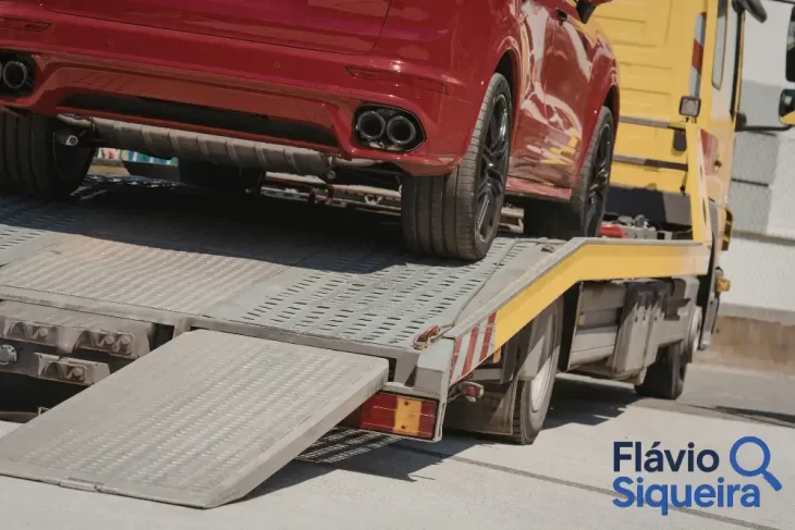 Busca e apreensão do veículo, carro vermelho sendo carregado em um caminhão-guincho, com rampa abaixada, sugerindo remoção do automóvel.